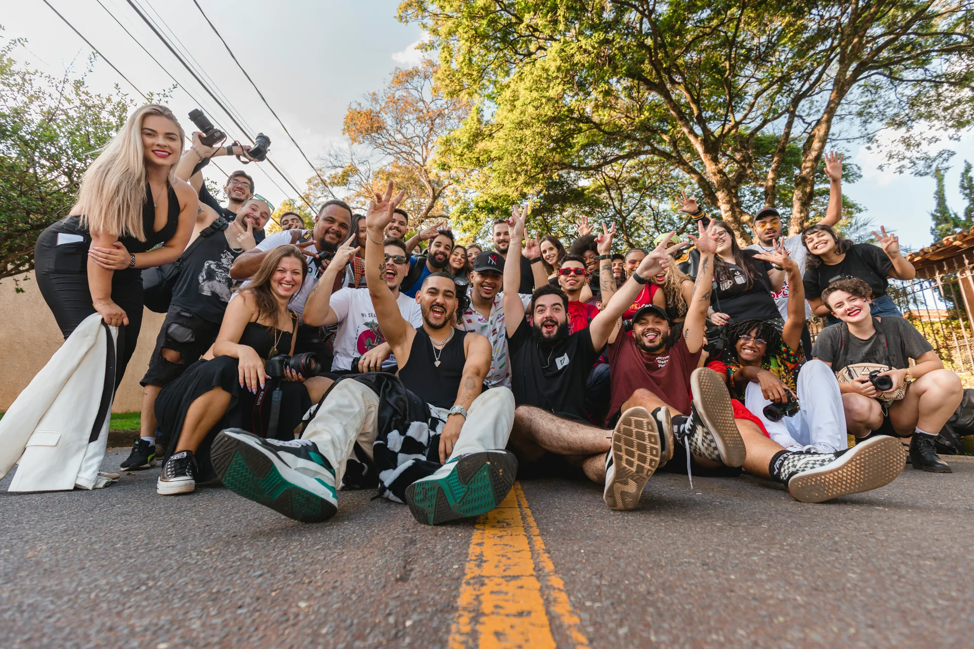 A large group of people seated together on a Cleveland street, smiling and raising their hands at a Recovery Grows community gathering.